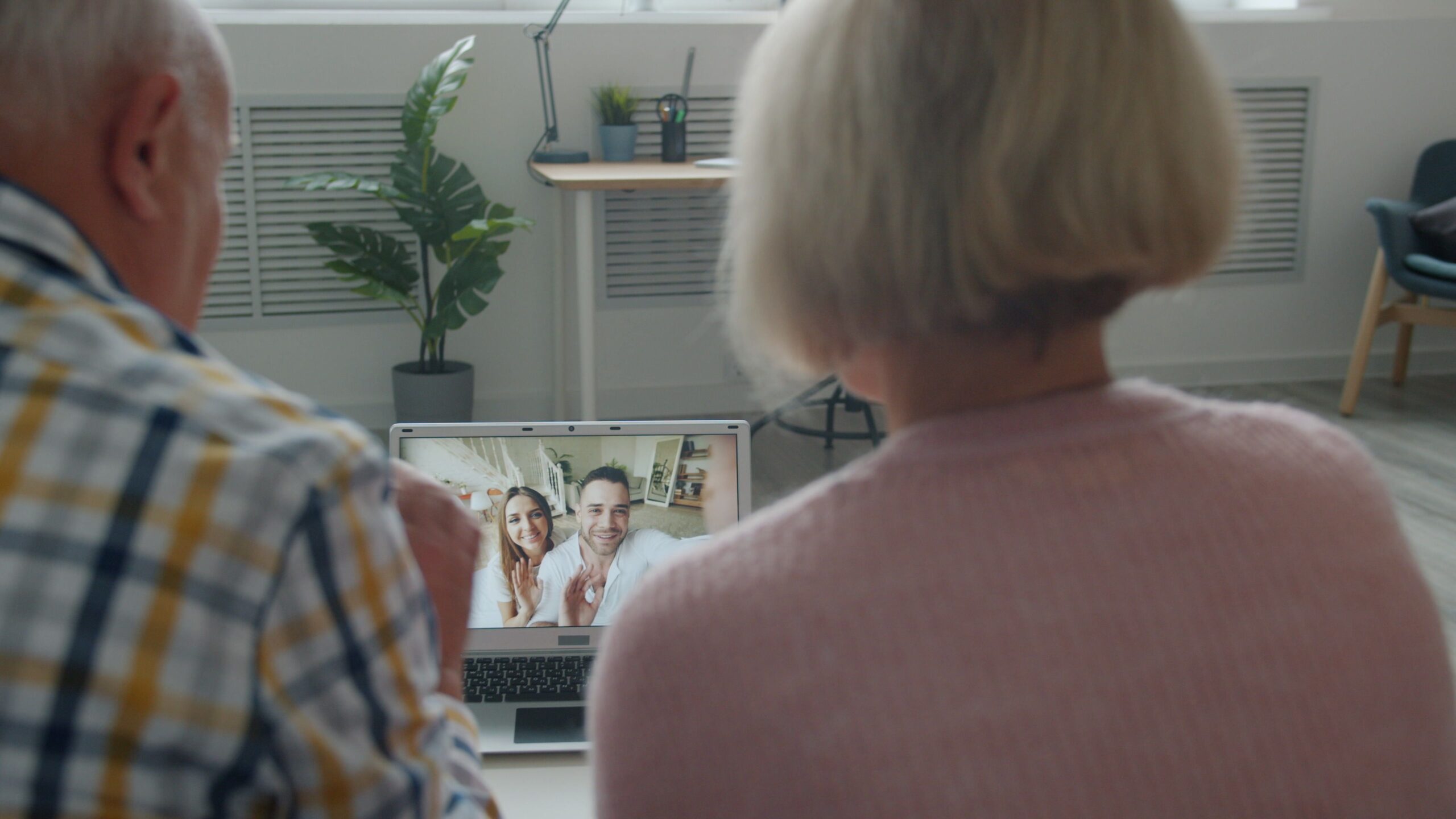 An elderly couple having a video call with family on a laptop at home.
